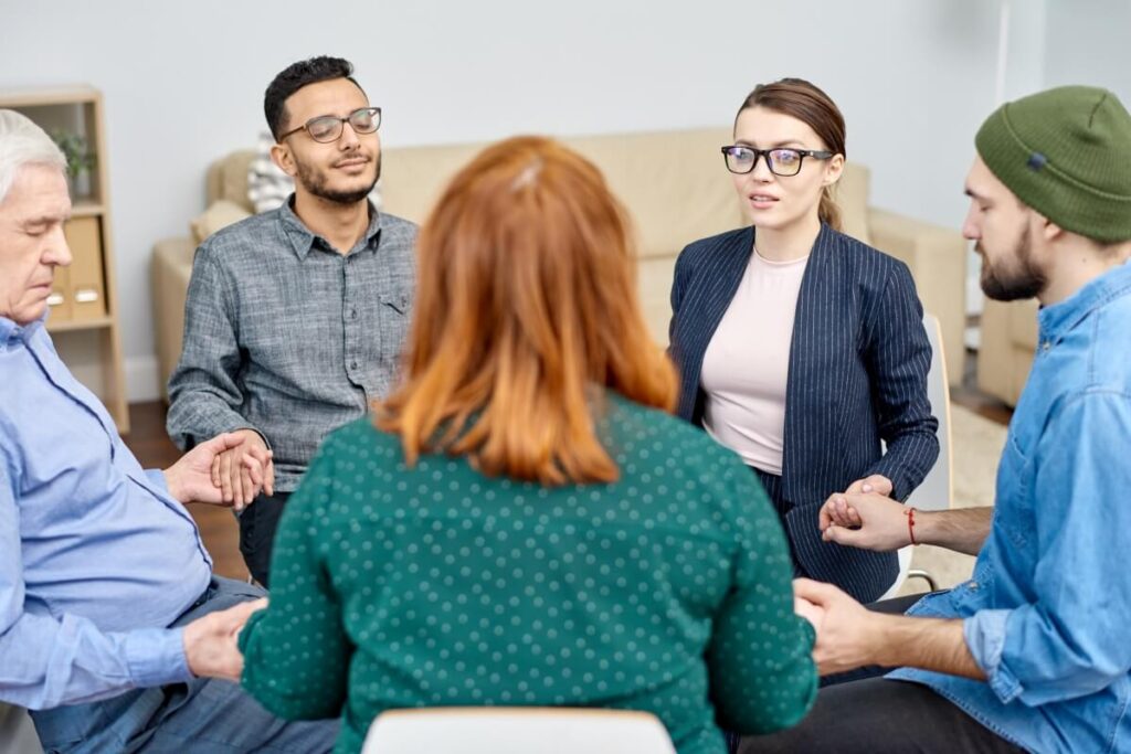 Grupa osób siedząca w kręgu podczas sesji terapeutycznej, dyskutująca o kosztach psychoterapii.