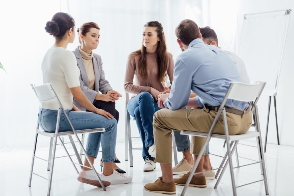 Grupa ludzi siedzi w kręgu, angażując się w terapię grupową prowadzoną przez dobrego psychoterapeutę.